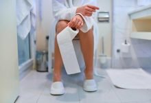 Mujer sosteniendo rollo de papel higiénico y sentada en el inodoro en el baño sin poder controlar la diarrea cáncer / ir al baño / infección sexual al usar un baño público / ir al baño - defecar