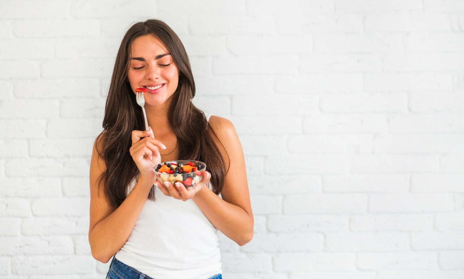 Mujer feliz comiendo una taza de frutas, sin fatiga ni cansancio / embarazo