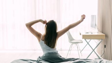 mujer joven que se extiende en la cama deshecha después de despertarse / despertar en la mañana / antes de dormir