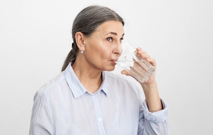 mujer senior expresiva posando mientras toma agua