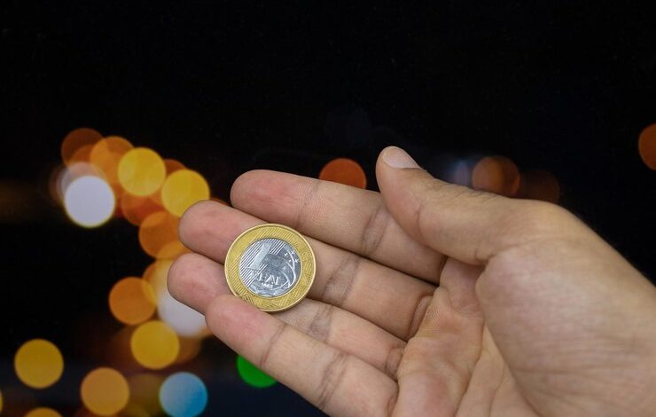 Foto sosteniendo una moneda de dinero brasileño en un fondo de luces borrosas