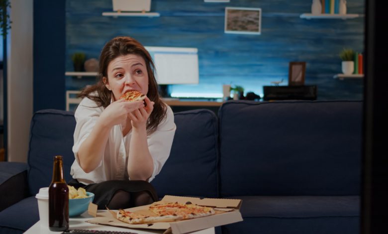 mujer joven comiendo pizza mientras mira la televisión