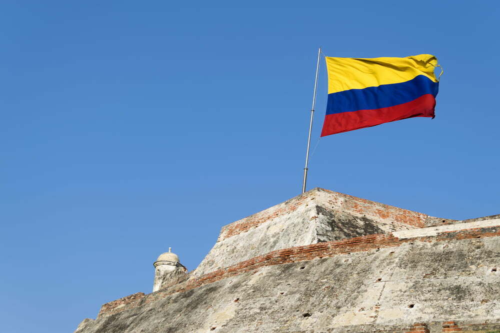 Una bandera colombiana ondea al viento sobre los muros erosionados de la fortaleza del Castillo San Felipe de Barajas en Cartagena de Indias, Colombia / Colombia / florero de Llorente / colombia