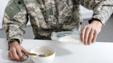 vista recortada del militar vertiendo leche en un tazón con copos de maíz / dieta militar