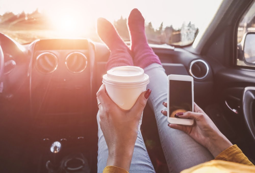 Mujer bebiendo taza de papel de café dentro del carro/ millennials