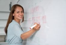 Educador feliz escribiendo instrucciones en tablero blanco / salario de docentes / vacantes