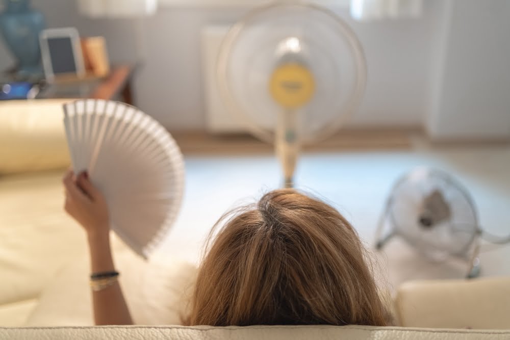 Mujer sentada en un sofá con varios fans dándole aire y un ventilador en la mano, altas temperaturas / Fenómeno de El Niño / calor