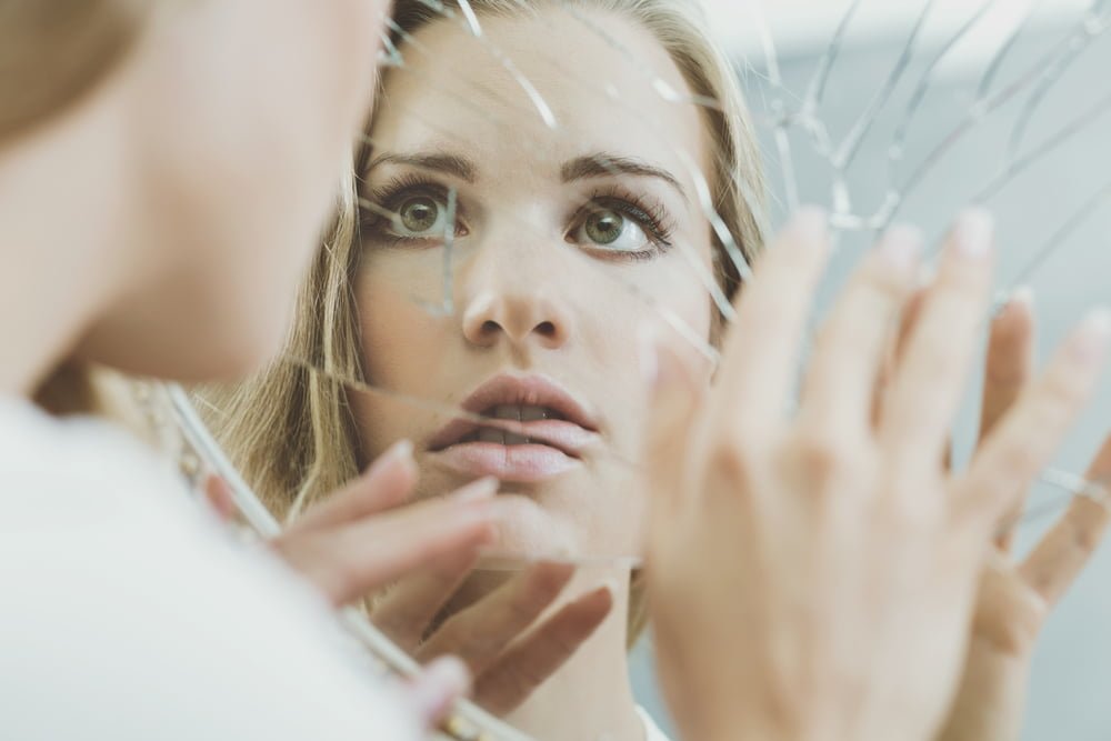 Rostro de mujer esquizofrénica reflejado en espejo roto / complejos