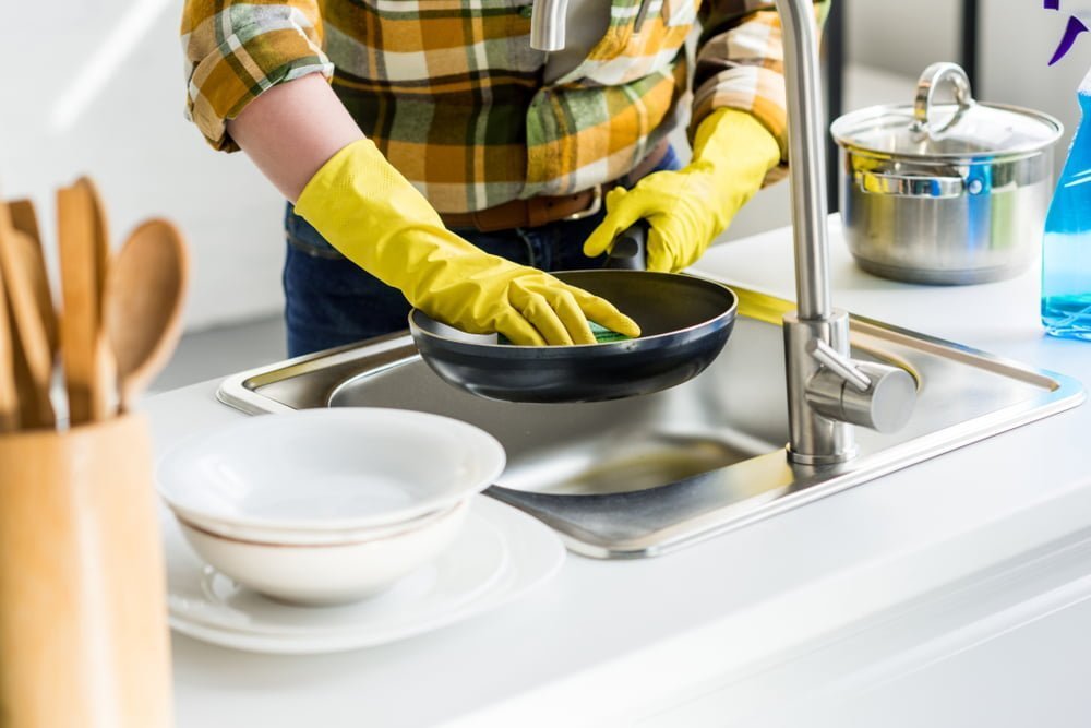 Imagen recortada de una mujer lavando una sartén en la cocina / olor a huevo